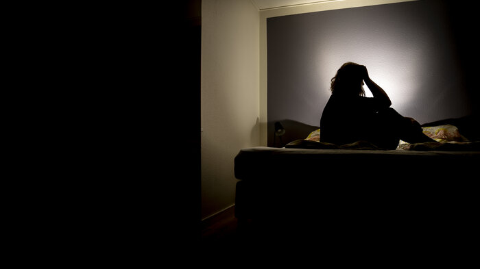 Illustrasjon av en person som sitter i mørket og har det vondt