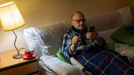 Bildet viser en eldre mann i sofaen hjemme.
