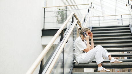 Bildet viser en sykepleier som sitter i en trapp og snakker i telefonen