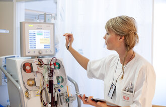 The photo shows an intensive care nurse touching a screen on a machine with tubes and other equipment.