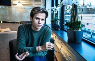 Bilde av studentleder som ser inn i kamera. Han holder briller i hånden.