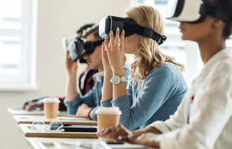 Bildet viser studenter med VR-briller på. De sitter ved sine pulter i et klasserom