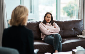 Bildet viser en person som sitter med ryggen vendt. Overfor henne sitter en ung jente som ser sint ut. Hun har armene i kors og et sint uttrykk i ansiktet.
