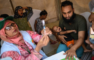 En helsearbeider forbereder en meslingvaksine for et lite barn i Bangladesh i april.
