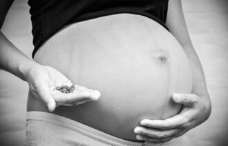Bildet viser en gravid mage og en hånd som holder mange piller.