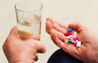 miljøterapi, psykisk helse, psykiatri Bildet viser to hender, den ene holder i et glass vann, den andre en håndfull tabletter.