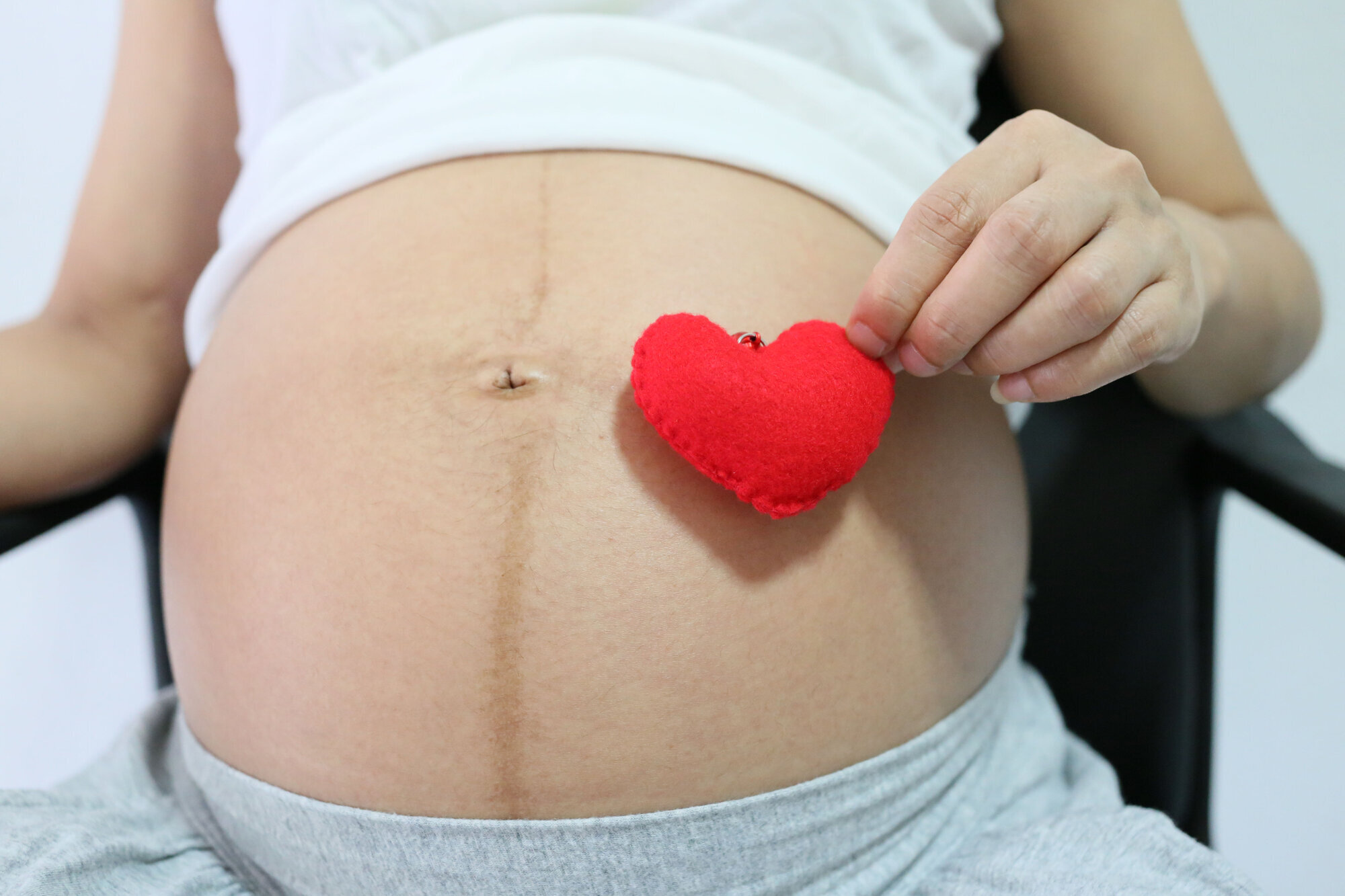 gravid, svangerskap, hjertehelse Bildet viser en gravid mage og en hånd som holder et tøyhjerte.