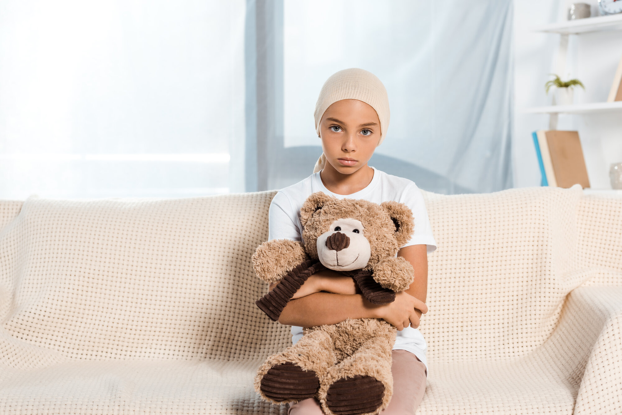 Sykt barn Bildet viser et sykt barn som sitter i en sofa og har en teddybjørn i fanget
