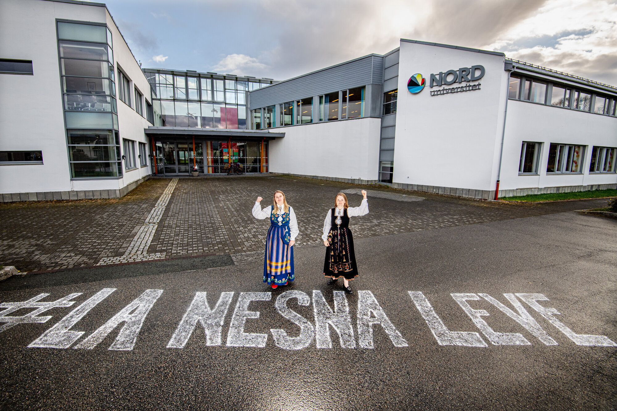 Nesna Bildet viser to bunadskledte mennesker utenfor høgskolen i Nesna, på bakken er det skrevet "La Nesna leve".