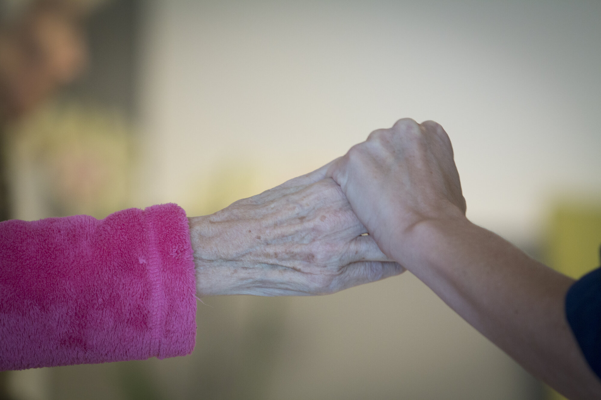 Bildet viser en sykepleier som holder et eldre menneske i hånden