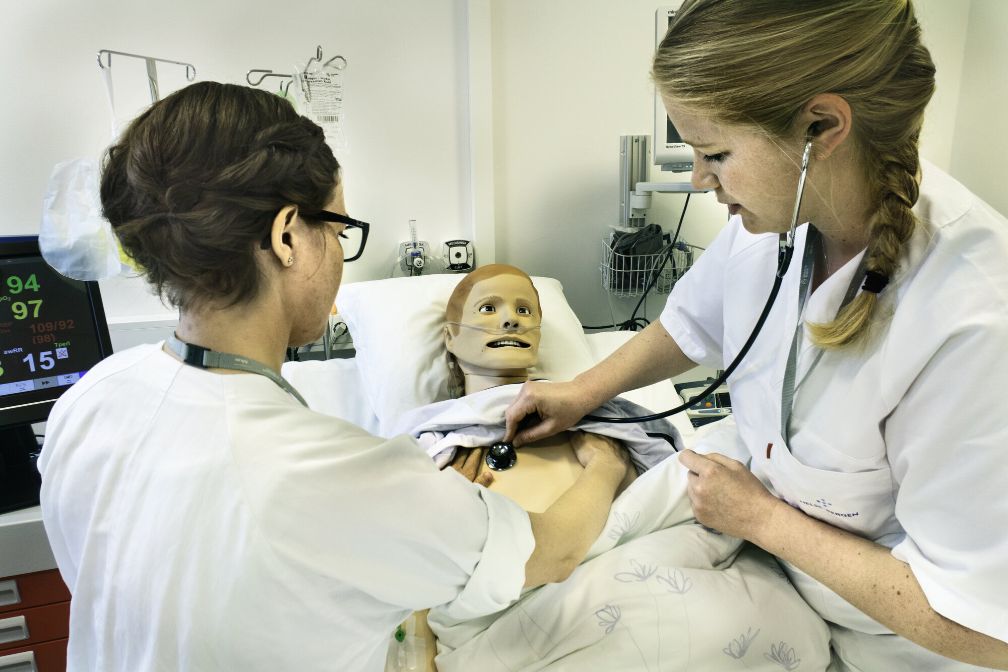 Simulering Bildet viser to sykepleiere som står ved en seng. I senga ligger en simuleringsdukke. Den ene sykepleieren lytter etter hjerteslag på dukken