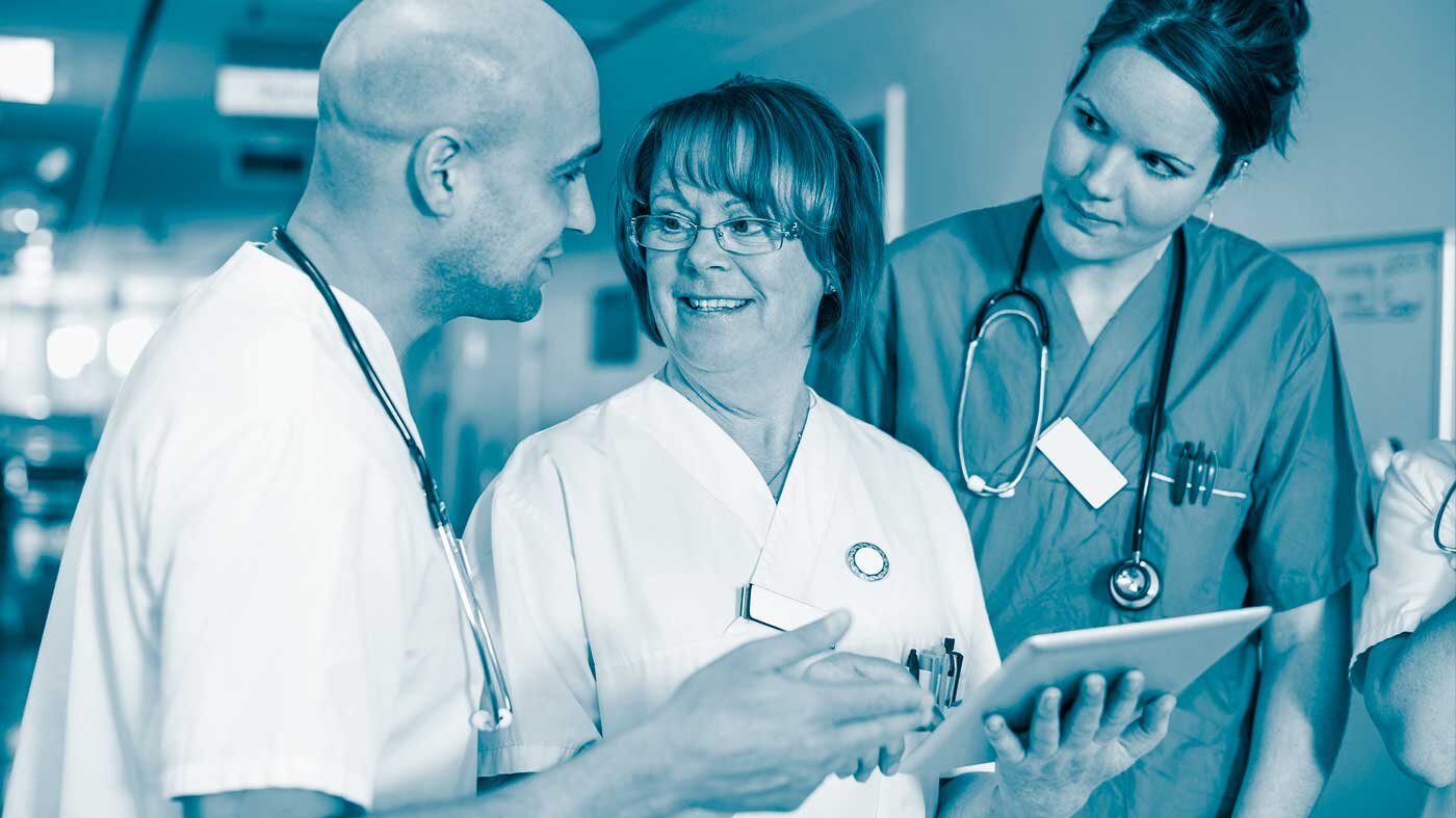 Health personell with form The photo shows three health professionals: a man and two women. The woman in the middle is holding a form. They are smiling at each other