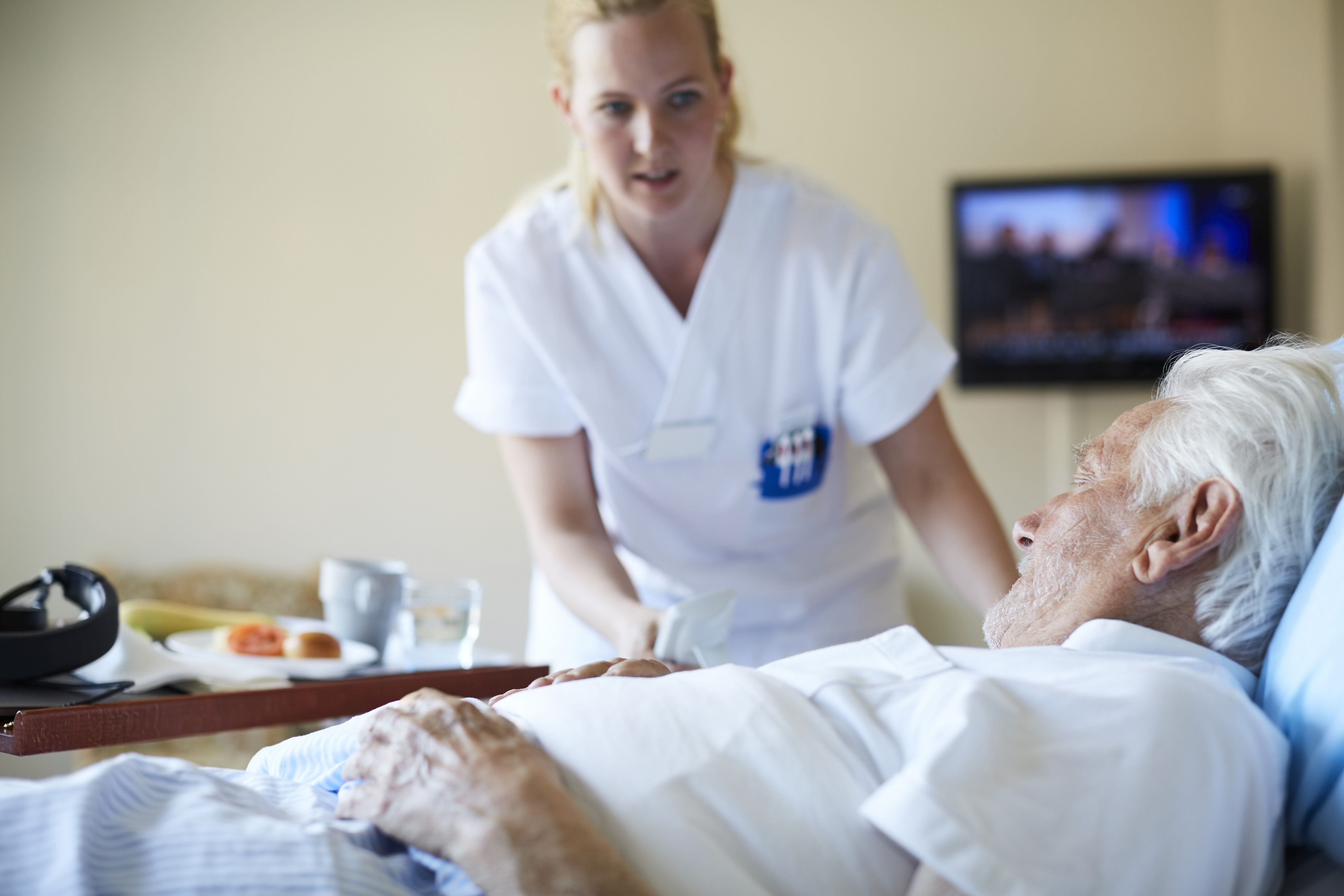 Municipal in-patient acute care unit The photo shows a nurse bending over a bed where an older man lies.