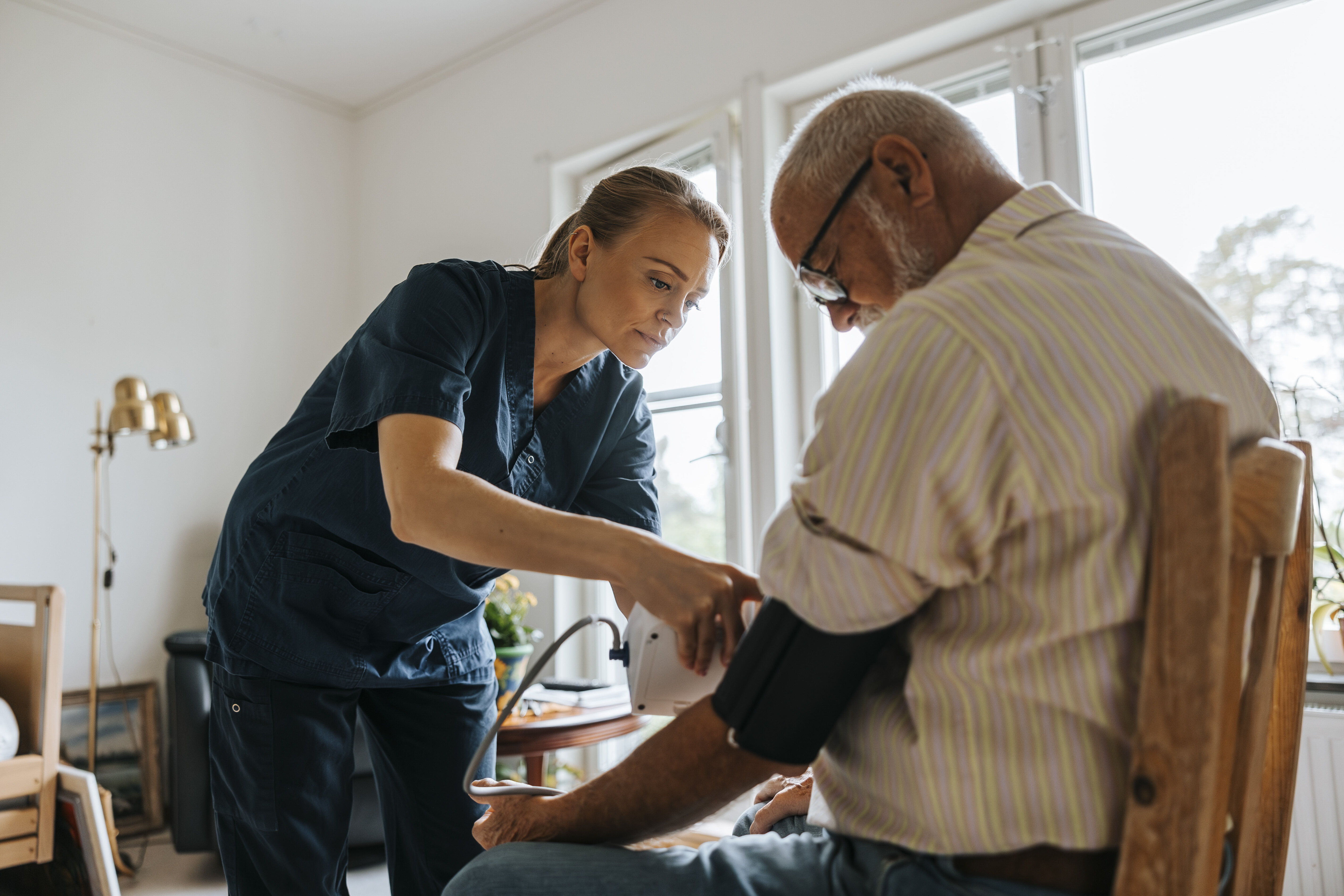 Nurse in home care services The image shows a nurse measuring the blood pressure of an elderly patient at home.