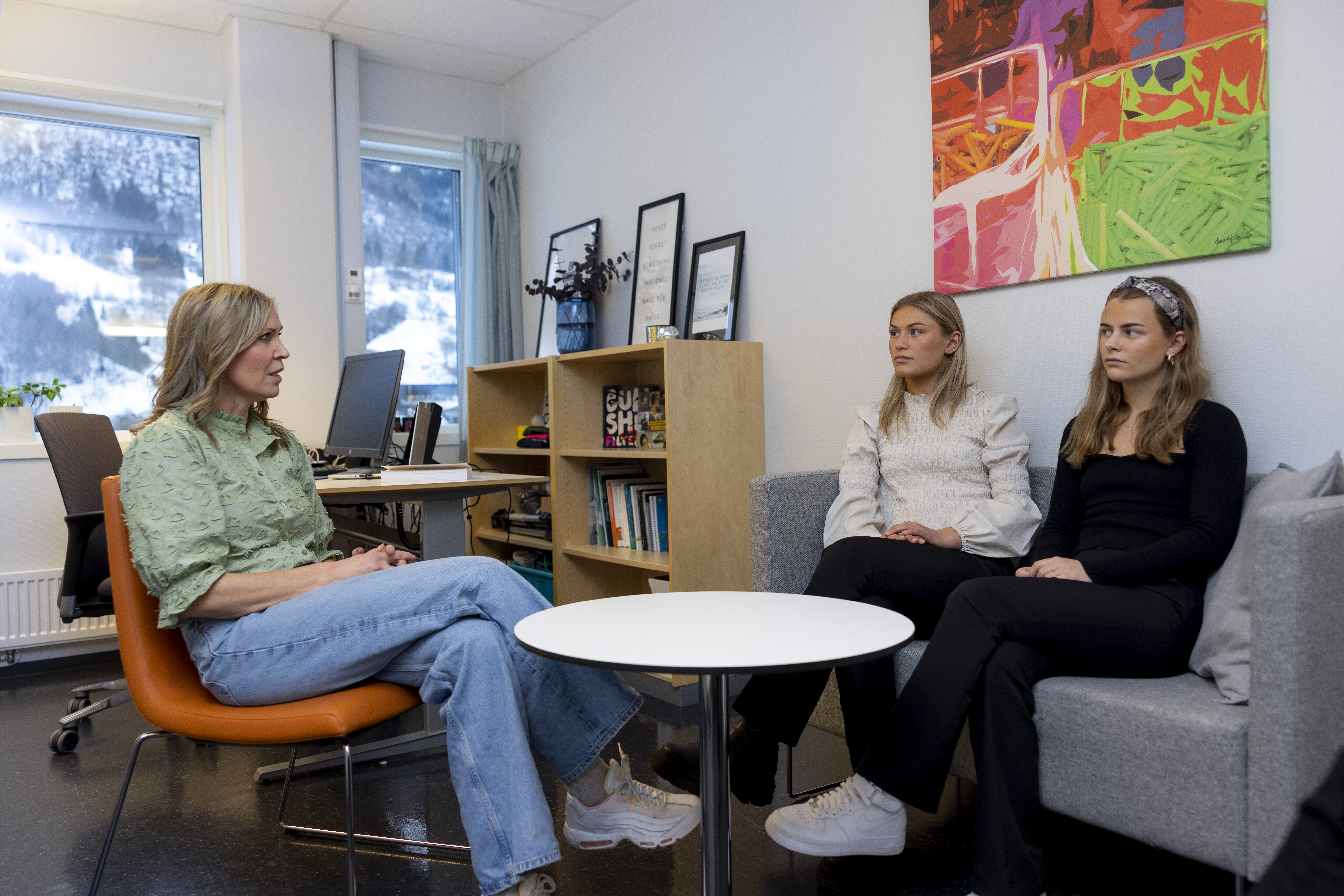 The photo shows a public health nurse in her office, sitting around a table with two teenage girls