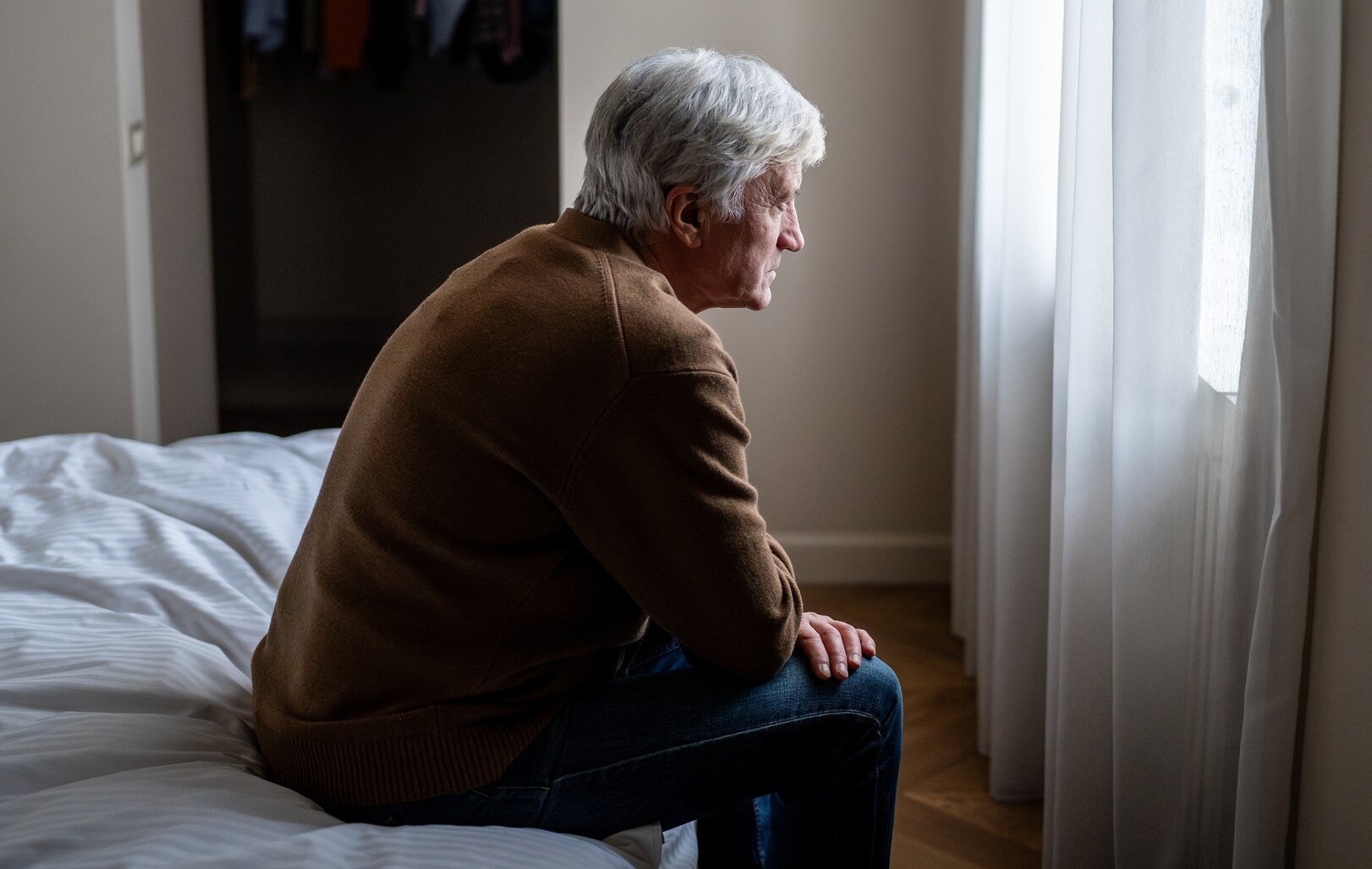 Bildet viser en deprimert mann som sitter alene på sengen