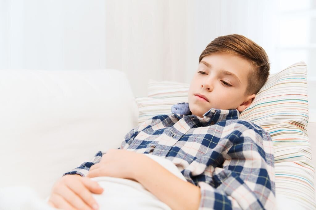 Barn Smerter Gutt med magesmerter som ligger på sofaen med et pledd over seg.