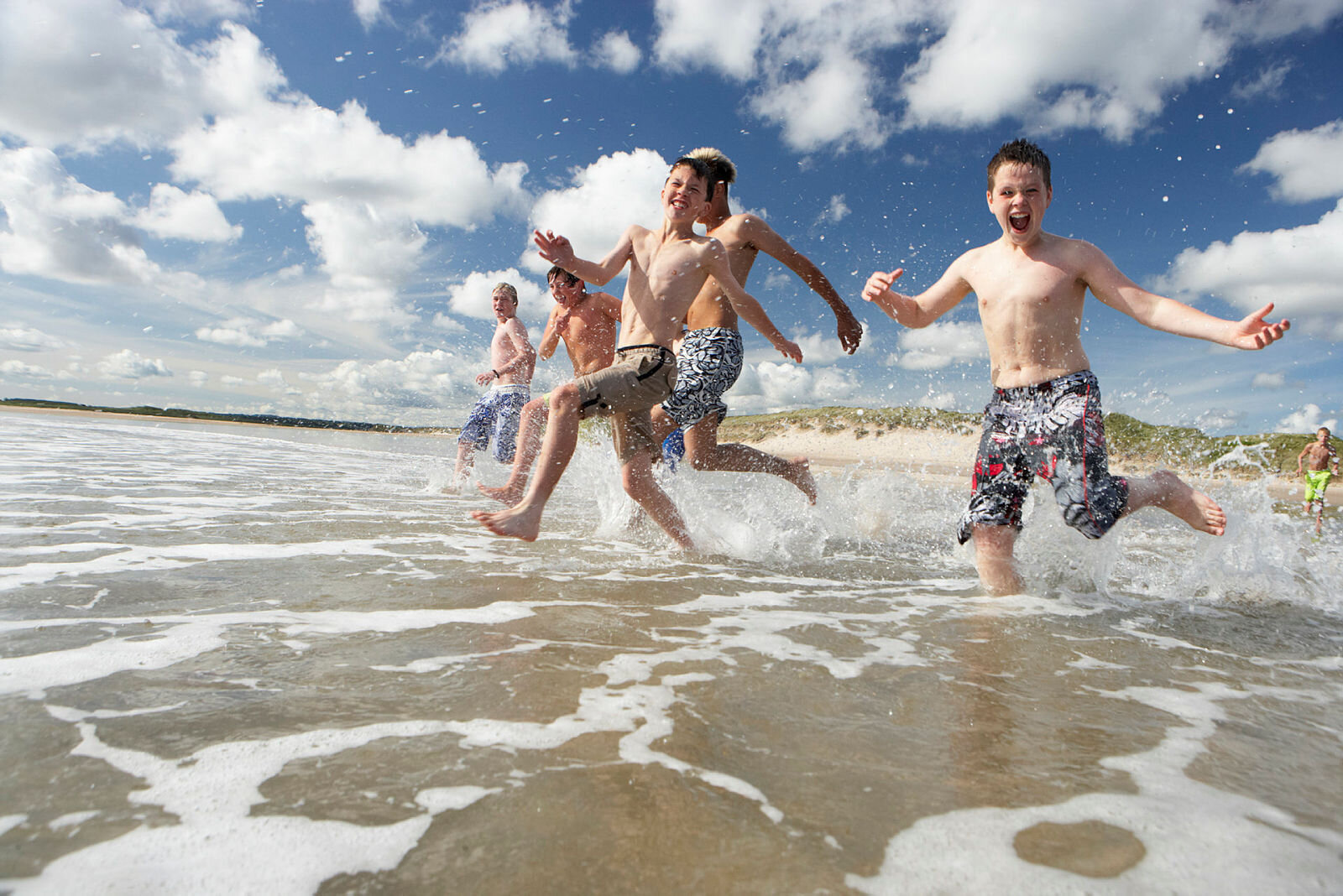 Bildet viser en gjeng med gutter som løper ut i vannet på en strand