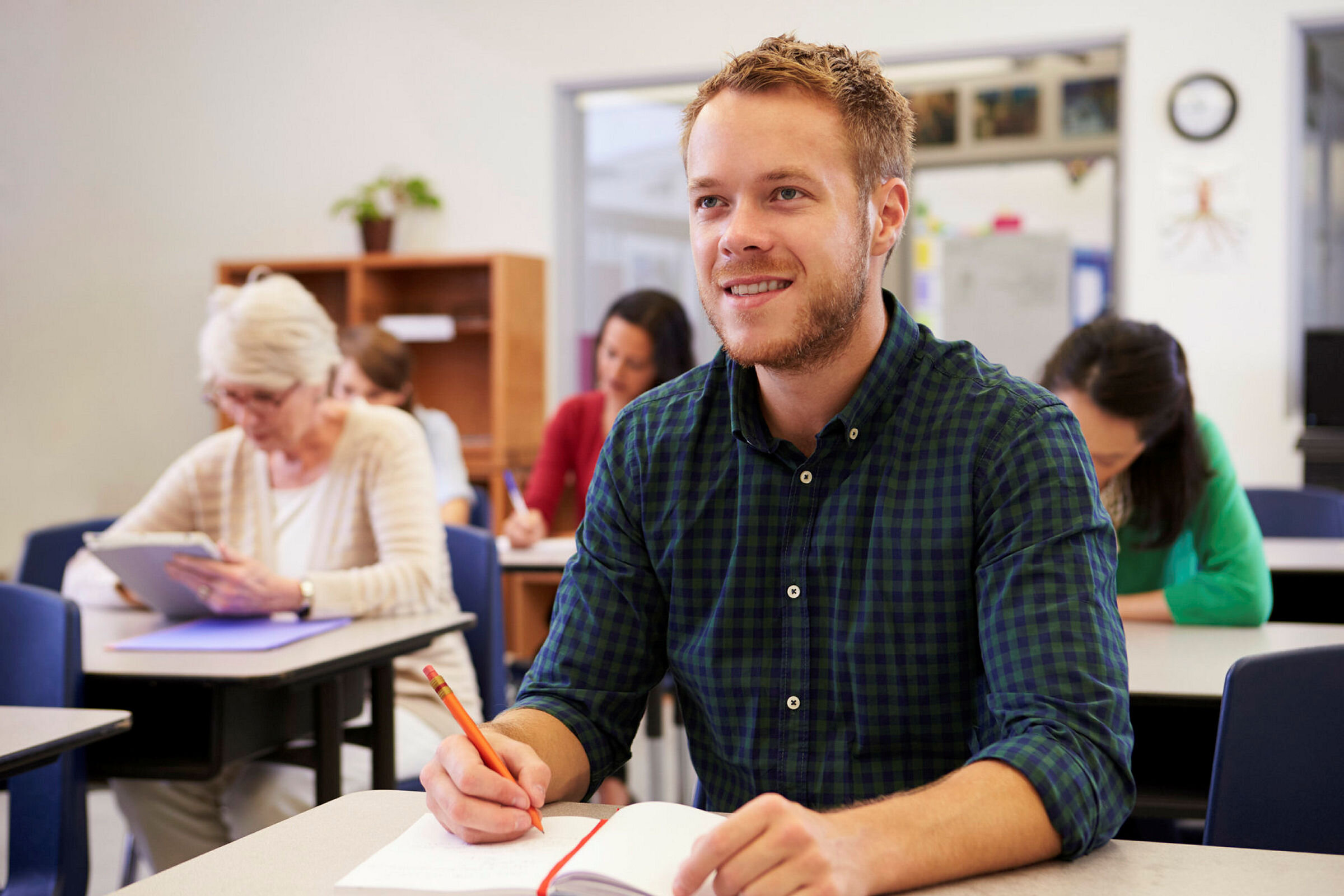 Klasseromsundervisning Bildet viser en ung mann i et klasserom. Det er flere studenter også i bakgrunnen.