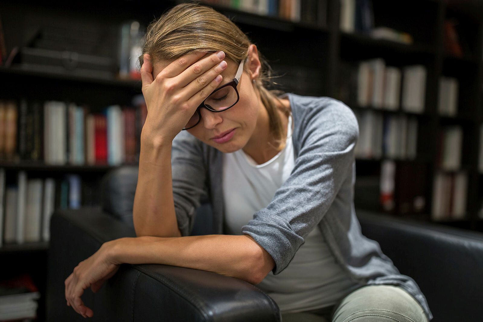 Bildet viser en kvinne som sitter i en stol og hviler pannen i hånden.