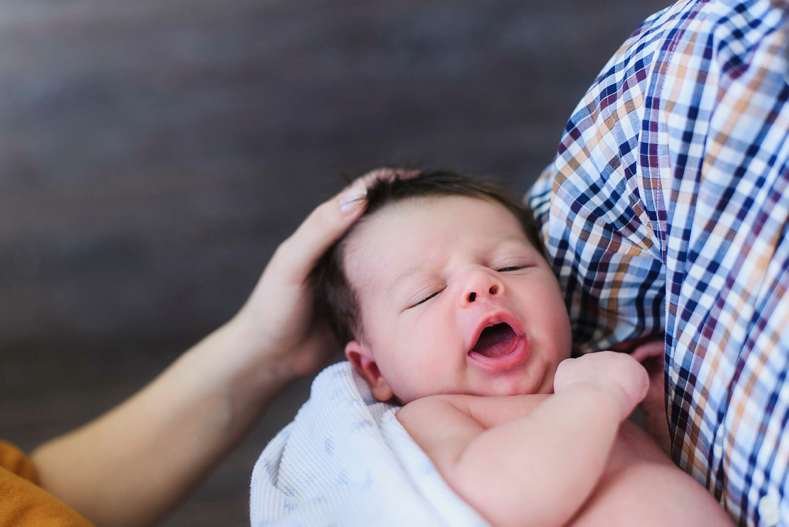 Baby Liten baby som gjesper mens han/hun får kos av mor og far.