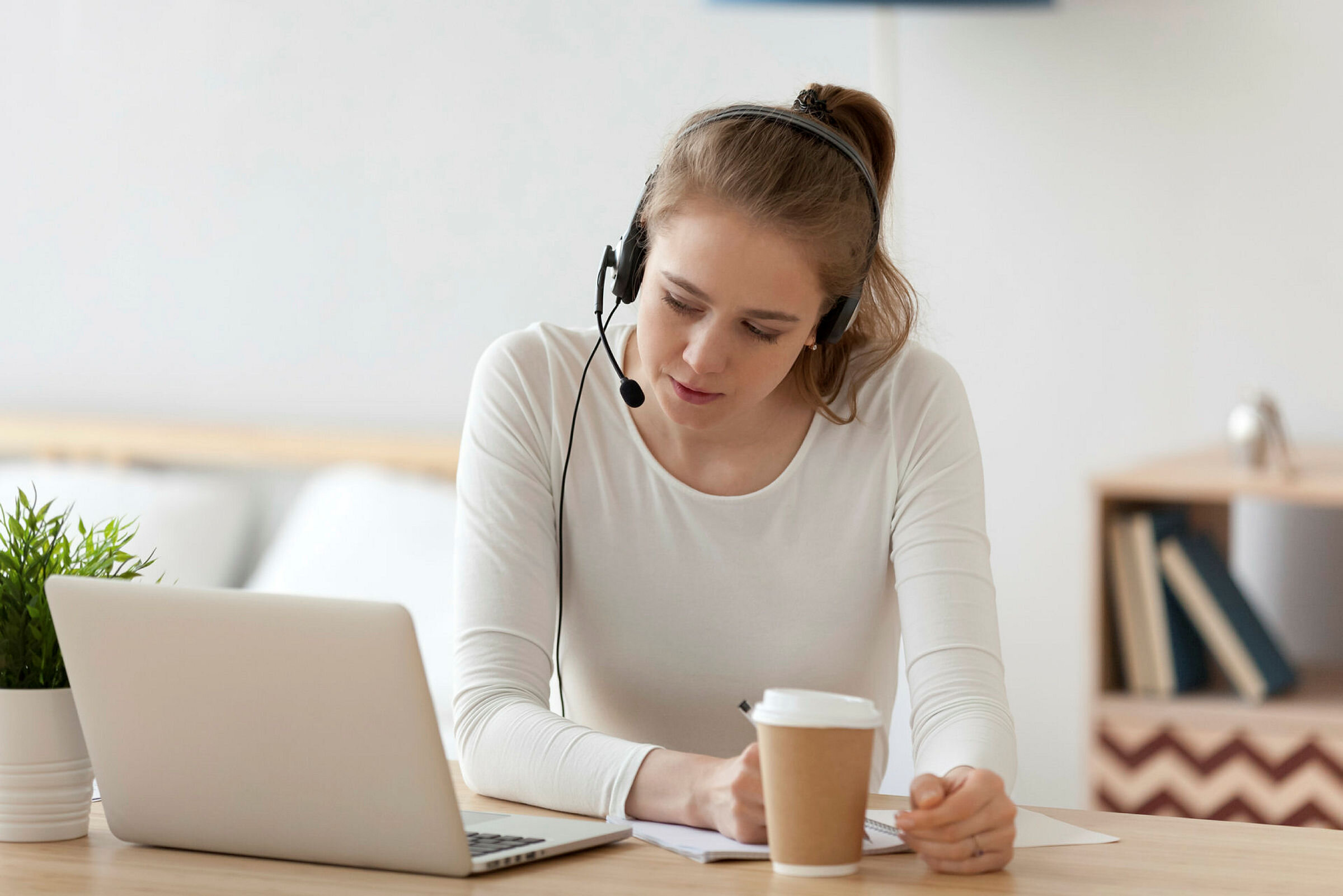 Ung kvinne studerer via Skype Bildet viser en ung kvinne som sitter i stua foran PC-en. Hun har hodetelefon med mikrofon på.