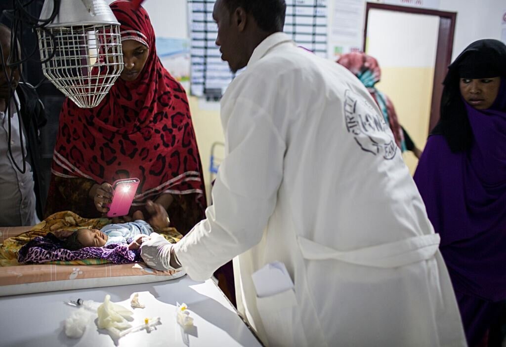Sykepleier Faduma Hassan lyser med lommelykta på mobilen når en av legene sliter med å finne blodåren på en nyfødt. Sykepleier Faduma Hassan lyser med lommelykta på mobilen når en av legene sliter med å finne blodåren på en nyfødt.