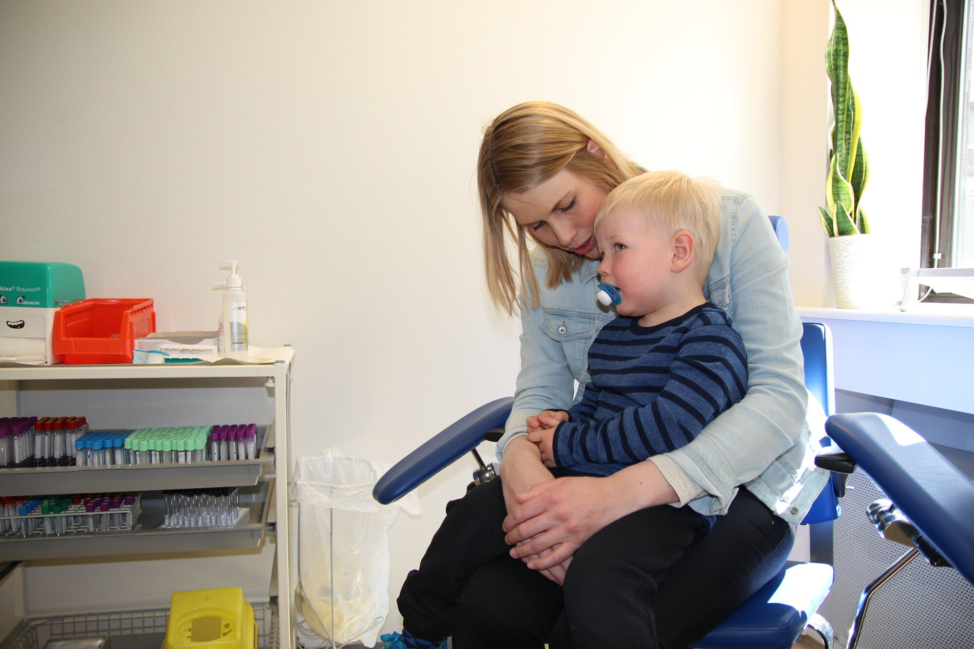 Sebastian gruer seg til blodprøven på sykehuslabben. Sebastian sitter på mammas fang og venter på blodprøve.