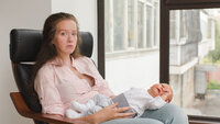 Bildet viser en nedstemt mor som sitter med babyen liggende på fanget
