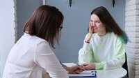 Tenåringsjente hos helsesjukepleiaren Bildet viser en tenåringsjente og helsesykepleier som sitter ved et lite bord. Helsesykepleieren har et skjema foran seg.