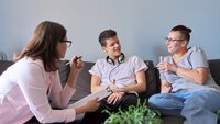 Samtale Bildet viser en ung gutt som sitter i en sofa og snakker med to kvinner