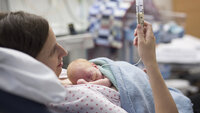 Bildet viser en kvinne på nyfødtintensiven. Hun ligger i sengen og mater sin nyfødte baby ved hjelp av sonde