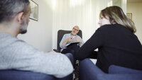 Terapisituasjon Bildet viser en mannlig terapeut som er vendt mot leseren. Foran ham sitter en mann og ei dame, som vi ser ryggen på.