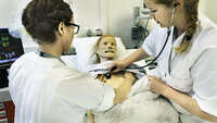 Simulering Bildet viser to sykepleiere som står ved en seng. I senga ligger en simuleringsdukke. Den ene sykepleieren lytter etter hjerteslag på dukken