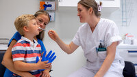 Nasal smertelindring til barn Bildet viser en liten gutt på fanget til sin mor. En sykepleier gir ham nesespray inn i det ene neseboret