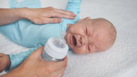 Crying infant The photo shows a crying infant. A soothing hand lies comforting on the baby's stomach. The other hand is holding a bottle ready to feed the baby