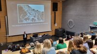 Bildet viser en foreleser som står foran mange studenter