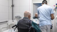 Bildet viser en mannlig sykepleier som steller en eldre pasient på badet