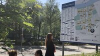 Bildet viser en dame som står foran et digert skilt foran St. Olavs hospital. Skiltet viser informasjon om sykehuset