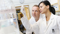 Laboratory The image shows a woman and a man in white laboratory coats holding a test tube with urine up to the light