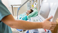 The photo shows nurse pressing monitor's button with male patient lying on bed in hospital