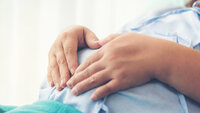 Bildet viser en kvinne som holder hender over en gravid mage.