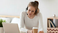Ung kvinne studerer via Skype Bildet viser en ung kvinne som sitter i stua foran PC-en. Hun har hodetelefon med mikrofon på.