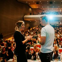 Bildet viser to studenter som står på scenen i et auditorium